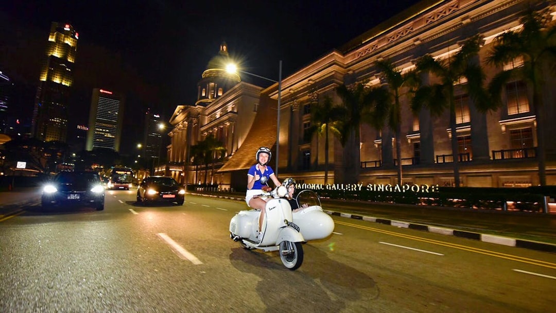 Person riding a vintage Vespa sidecar past the National Gallery in Singapore at night.