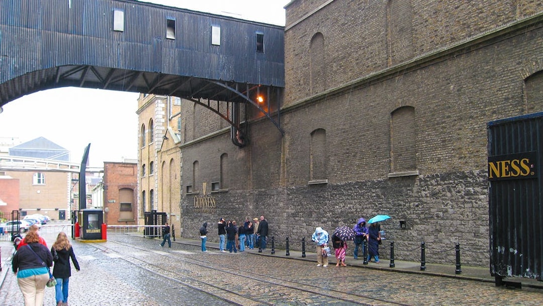 Guinness Storehouse exterior with visitors walking on cobblestone street in Dublin.