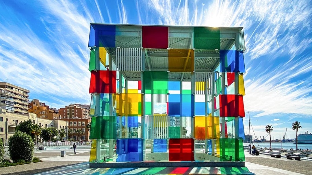 Colorful glass cube structure at Centre Pompidou Malaga with cityscape and sky in the background.
