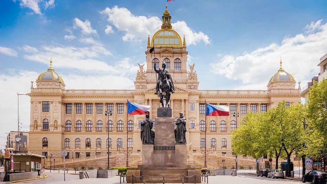 Prague National Museum with equestrian statue and Czech flags in front.