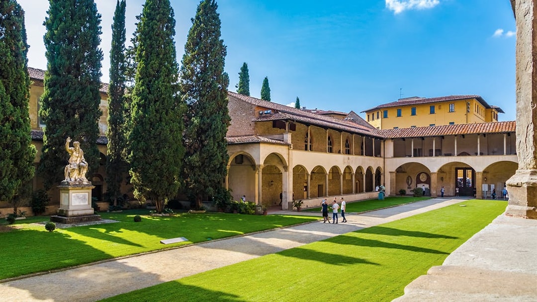 Cloisters of Santa Croce Basilica Complex with statue and visitors in Florence, Italy.