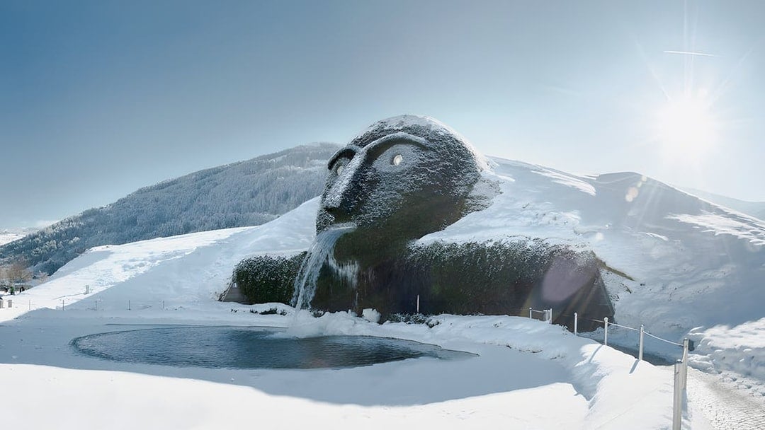 Giant head sculpture with waterfall at Swarovski Crystal Worlds, Austria, in snowy landscape.