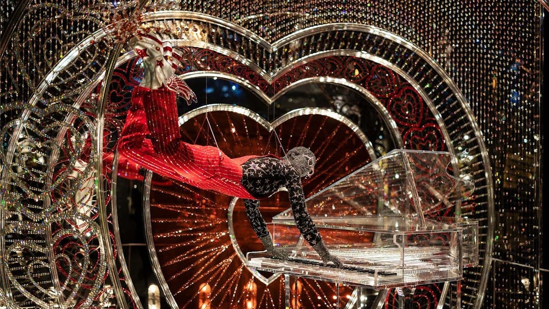 Performer in Swarovski Crystal Worlds display with crystal piano and heart backdrop.