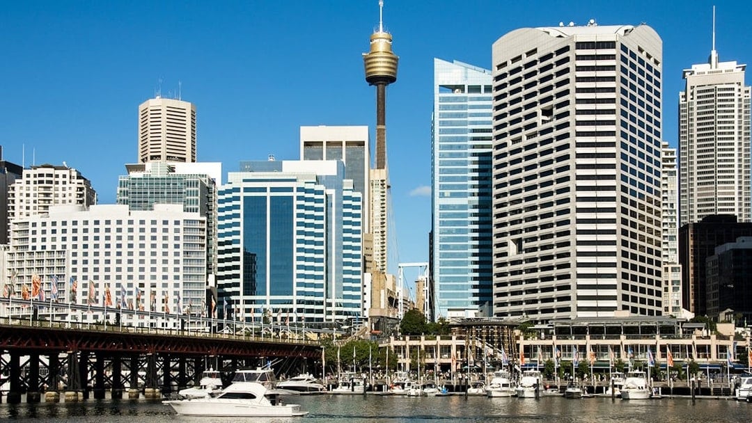 Sydney Tower rising above city skyline with boats in Darling Harbour.
