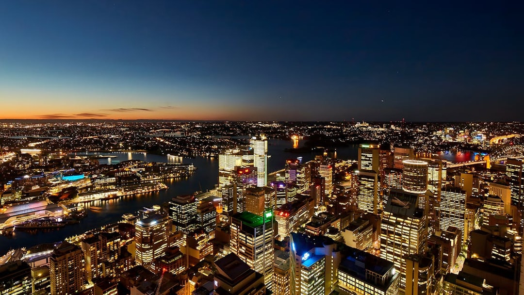 Sydney cityscape at dusk viewed from SkyFeast at Sydney Tower, with illuminated buildings and harbor.