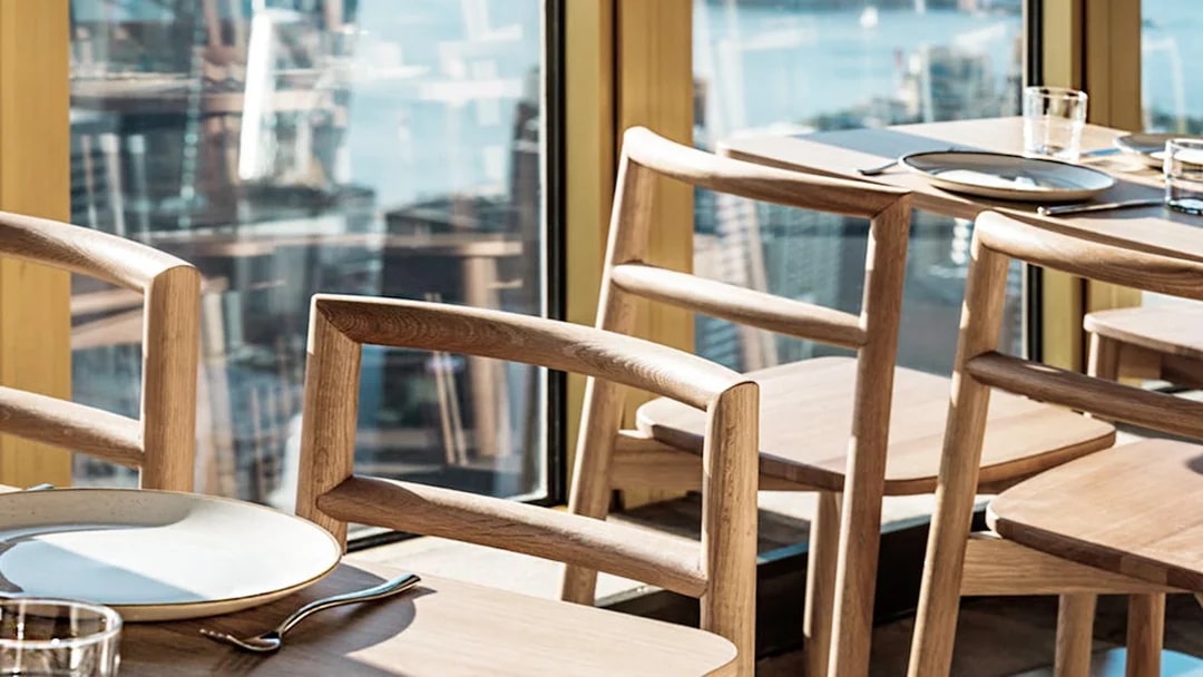 Dining setup with wooden chairs and table at SkyFeast, Sydney Tower, overlooking cityscape.