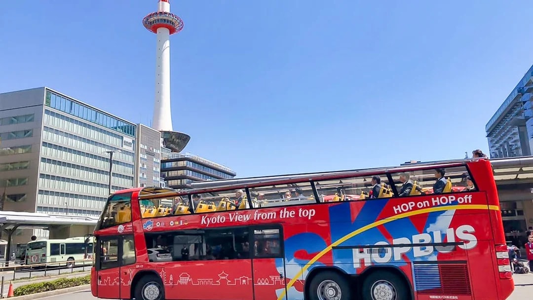 Kyoto Sky Hop Bus passing Kyoto Tower on a clear day.