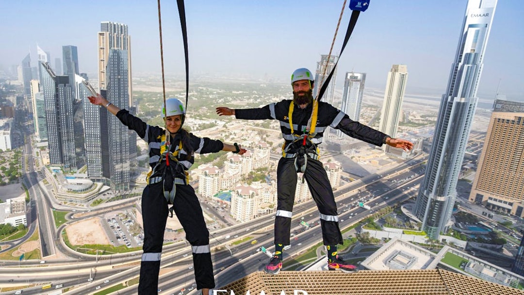 Participants on Edge Walk at Sky Views Observatory, Dubai, with city skyline in background.