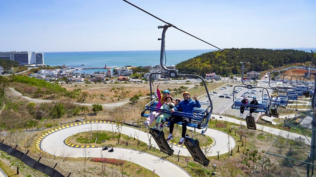 Family on chairlift at Skyline Luge Busan with coastal view in background.