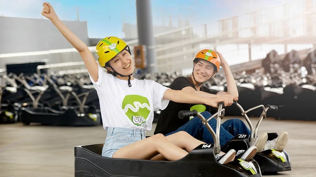 Two people enjoying a ride at Skyline Luge Busan, wearing helmets and smiling.
