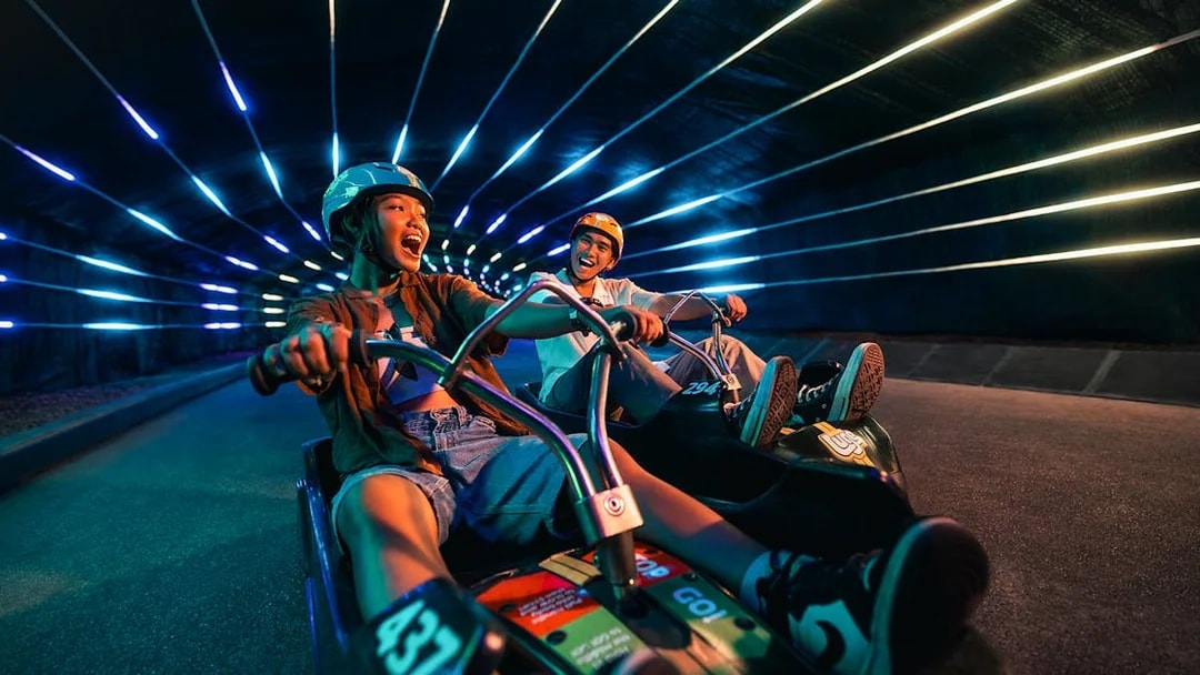 Two people enjoying a luge ride in a neon-lit tunnel at Skyline Luge Singapore.