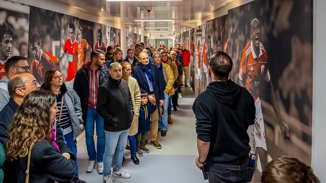 Visitors on a guided tour at Benfica Stadium museum hallway with player murals.