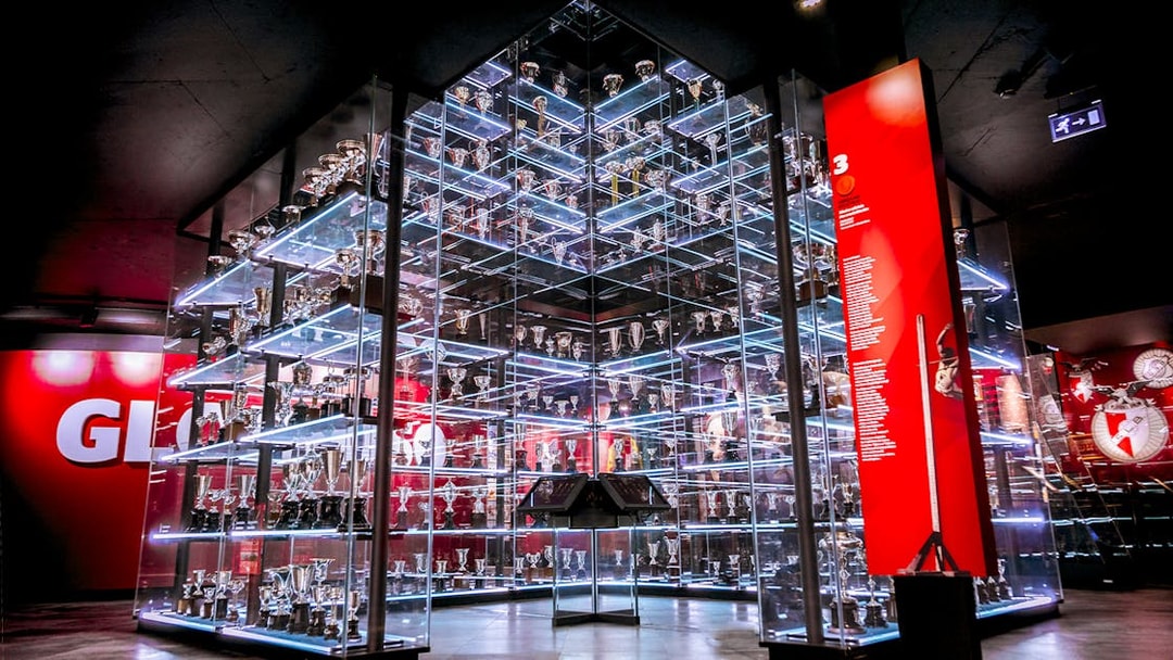 Benfica Stadium Museum trophy display with glass shelves and red backdrop.