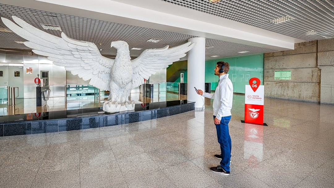 Man observing large eagle statue in Benfica Stadium's eagle hall, Lisbon.