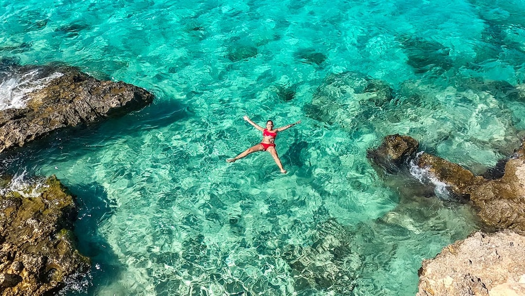 Person floating in clear turquoise water near rocky shore, Gozo and Comino cruise.