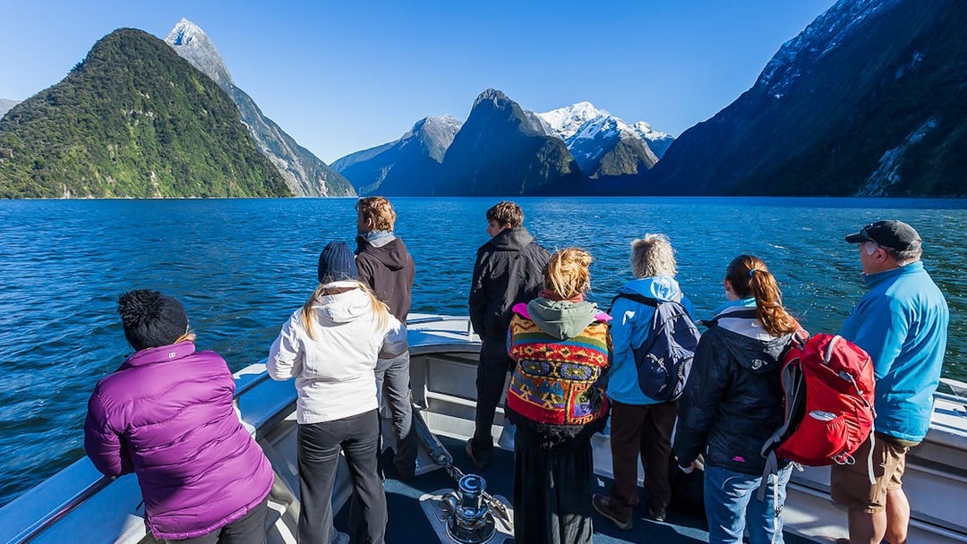 Tourists on a cruise at Milford Sound, viewing the fjord's towering cliffs and clear waters.