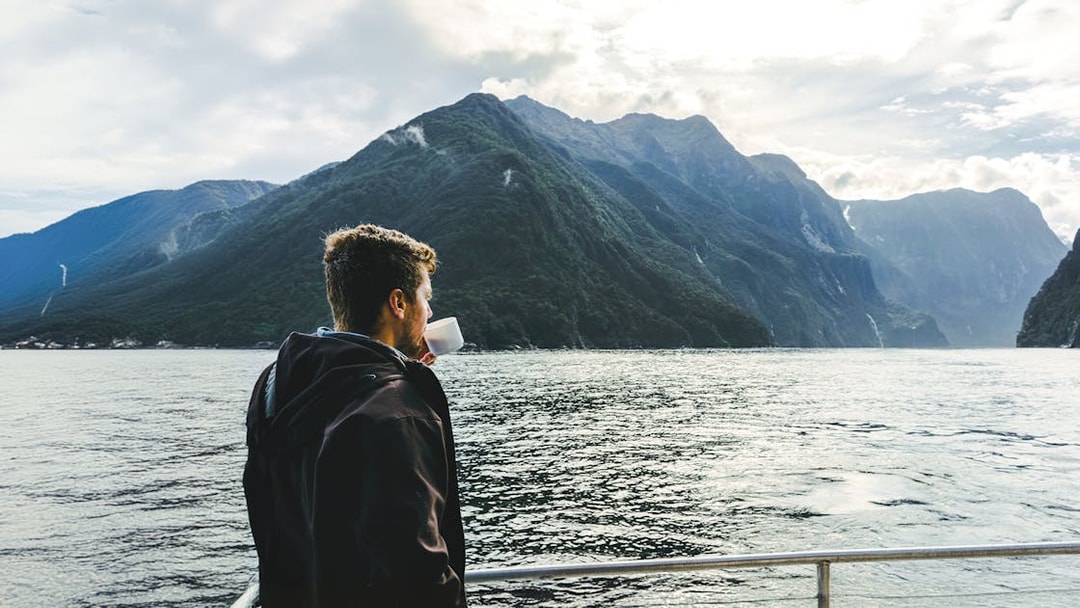 Person enjoying a drink on a Milford Sound cruise with mountain views.