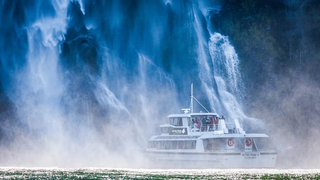 Cruise boat near waterfall at Milford Sound, New Zealand.