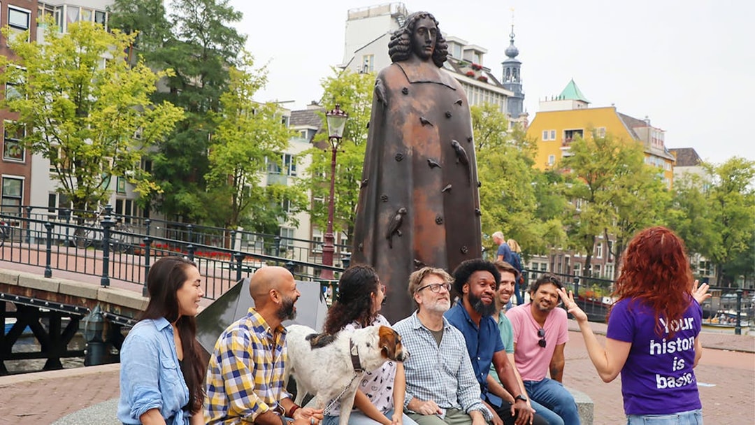 Group tour near a statue in Amsterdam with a guide explaining.
