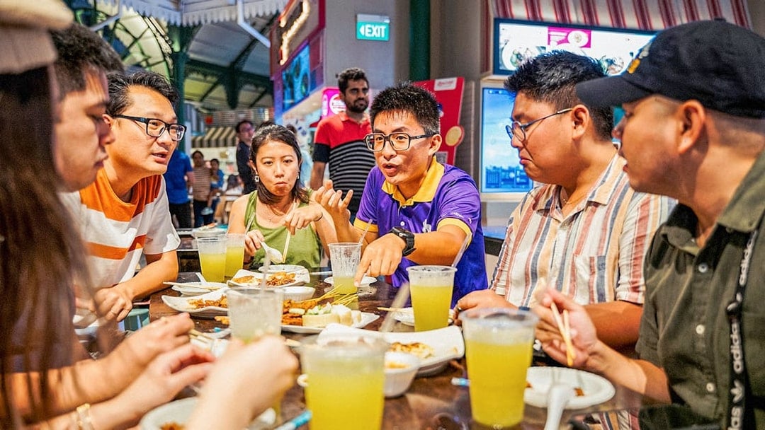 Group enjoying Singapore street food at a night market table.