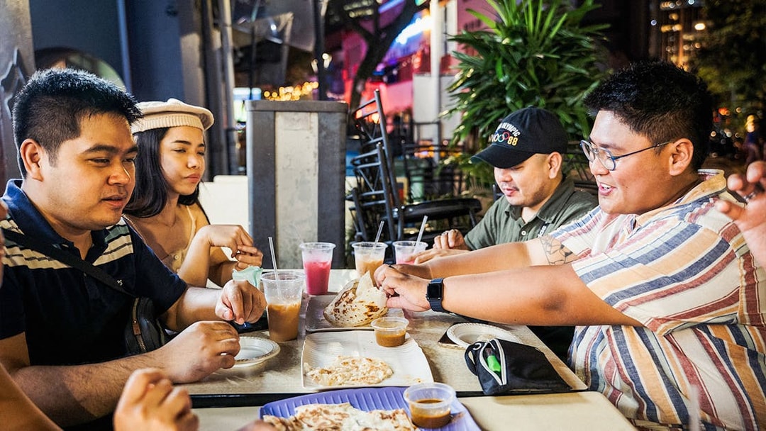 Group enjoying roti prata and drinks at a Singapore street food night market.