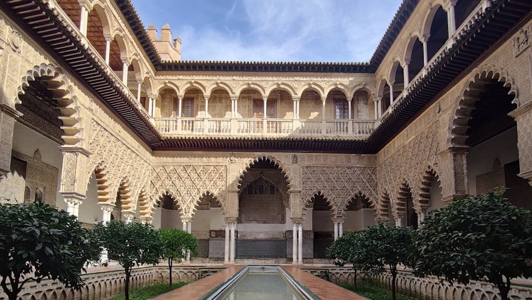 Alcázar courtyard with intricate arches and reflecting pool, Seville.