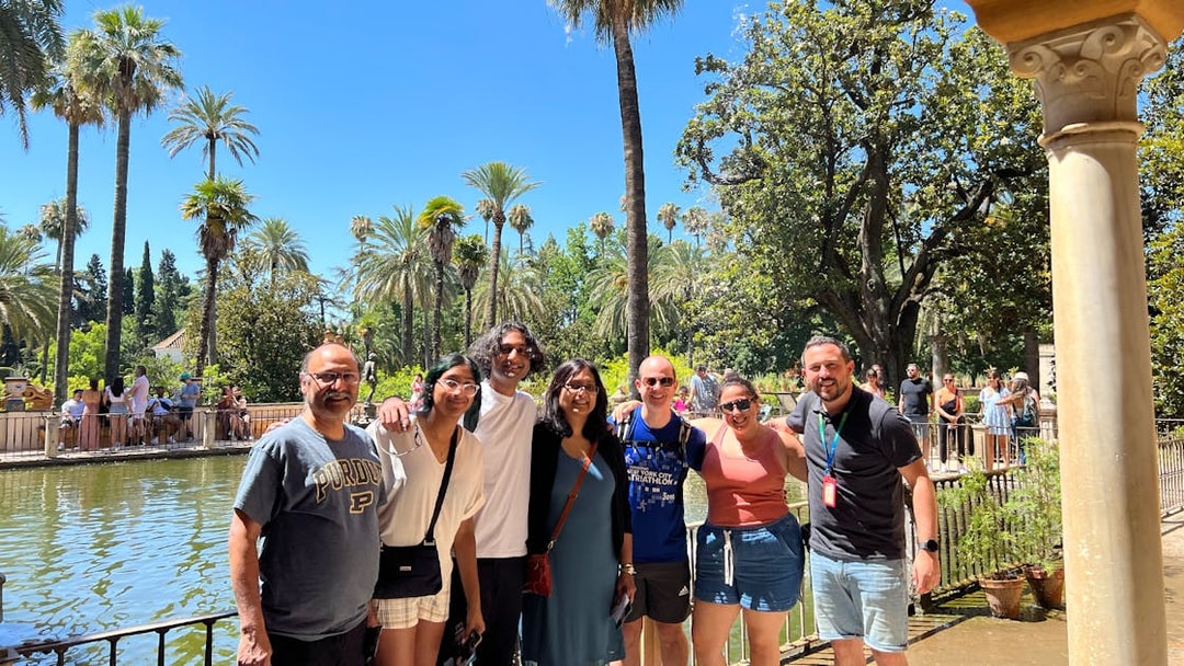 Group of tourists at the Alcázar gardens in Seville, Spain, with palm trees and a pond.