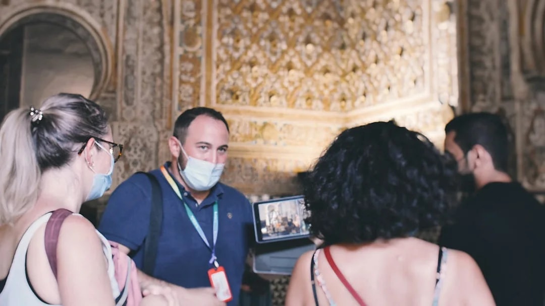 Visitors on a guided tour inside the Alcázar, observing intricate wall details.