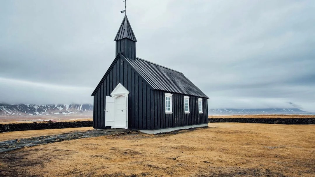 Black church on Snaefellsnes Peninsula with mountains in the background.