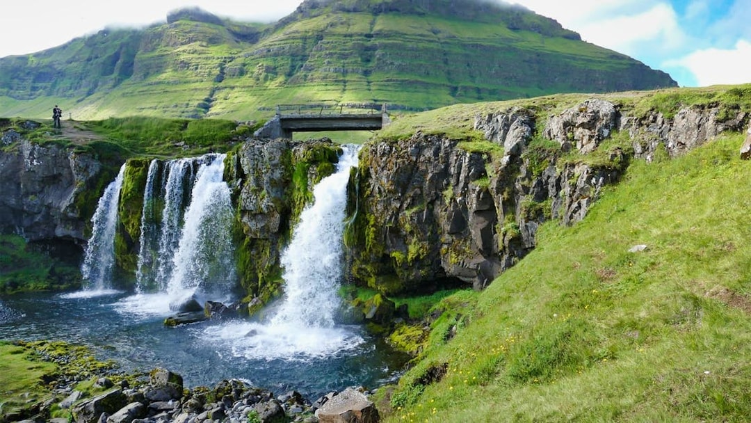 Waterfall on Snaefellsnes Peninsula with lush green cliffs and a mountain backdrop.