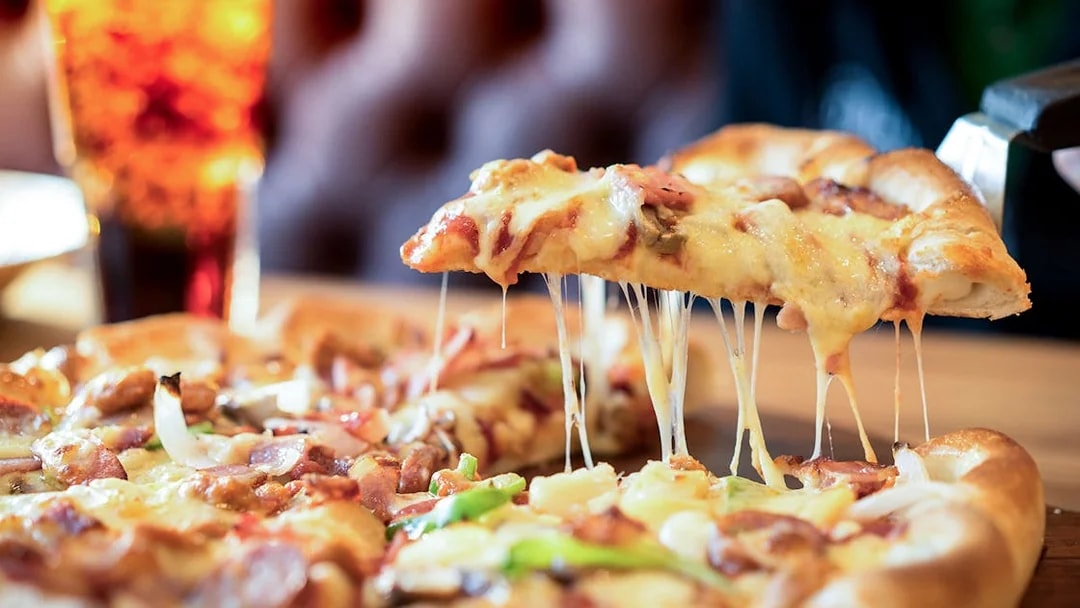 Cheese pizza slice being lifted with a drink in the background.