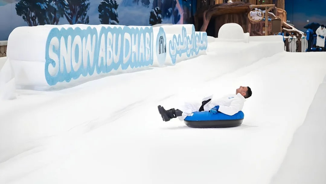 Person tubing down snowy slope at Snow Abu Dhabi indoor park.