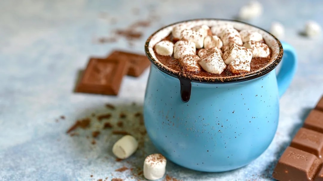 Hot chocolate with marshmallows in a blue mug, surrounded by chocolate pieces.