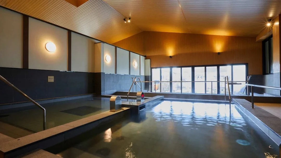 Indoor hot spring bath at Solaniwa Onsen with wooden ceiling and large windows.