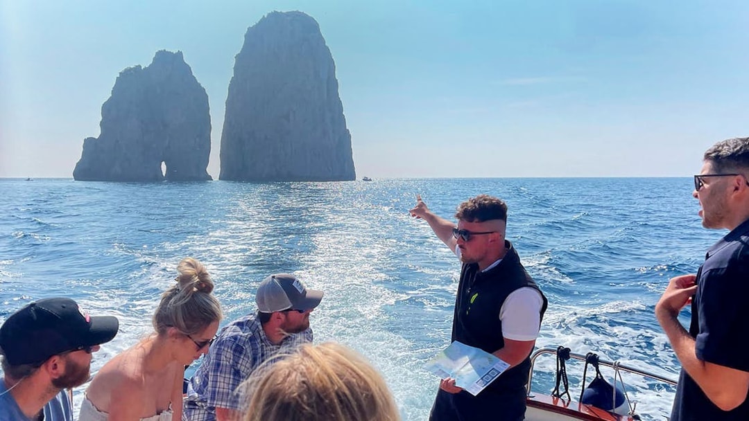 Tour group on boat near Faraglioni rocks, Capri, with guide pointing, part of Capri & Anacapri tour.
