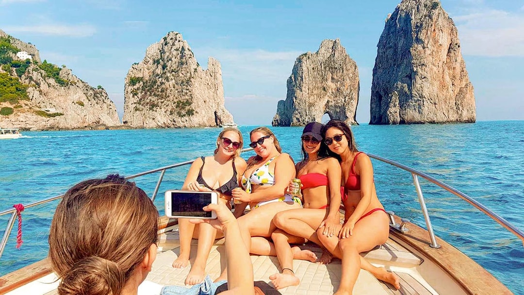 Tourists on a boat near Faraglioni rocks, Capri, during Capri & Anacapri with Blue Grotto tour.
