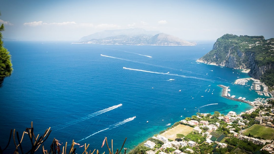 Aerial view of Capri coastline with boats in the sea, showcasing lush cliffs and marina.