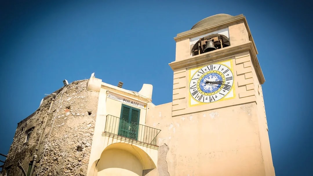 Clock tower in Capri, Italy, with Roman numerals and bell, part of Capri & Anacapri tour.