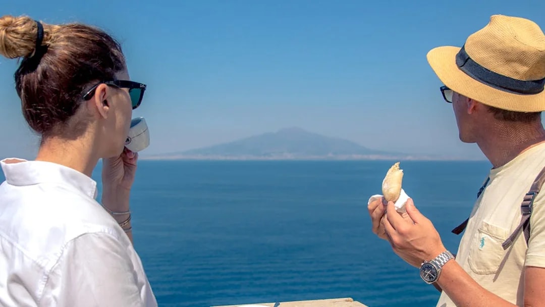 Tourists enjoying coffee and pastry with a view of Mount Vesuvius on a Sorrento walking tour.