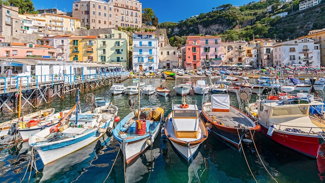 Boats docked at Marina Grande with colorful buildings in Sorrento, Italy.