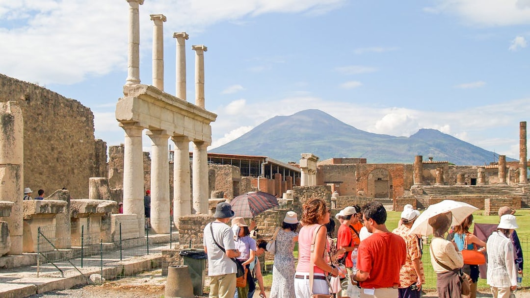 Tour group with guide exploring ancient ruins of Pompeii, Naples, with Mount Vesuvius in background.