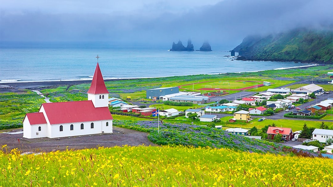 Church with red roof in Vik, Iceland, overlooking ocean and Reynisdrangar sea stacks.