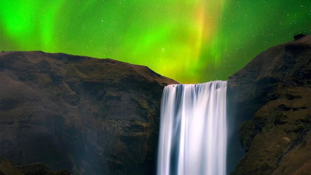 Skógafoss Waterfall in Iceland with northern lights in the sky.