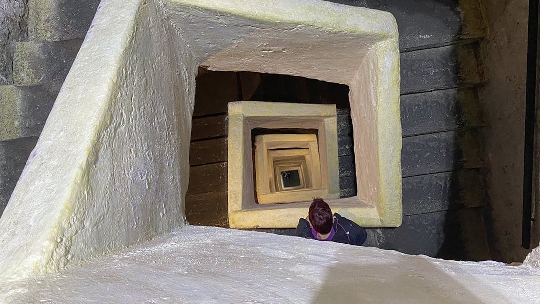 Naples Underground staircase with person descending through square stone passage.