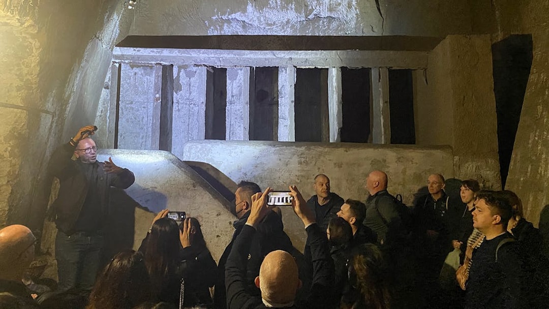 People exploring ancient walls during a guided tour in Naples underground.
