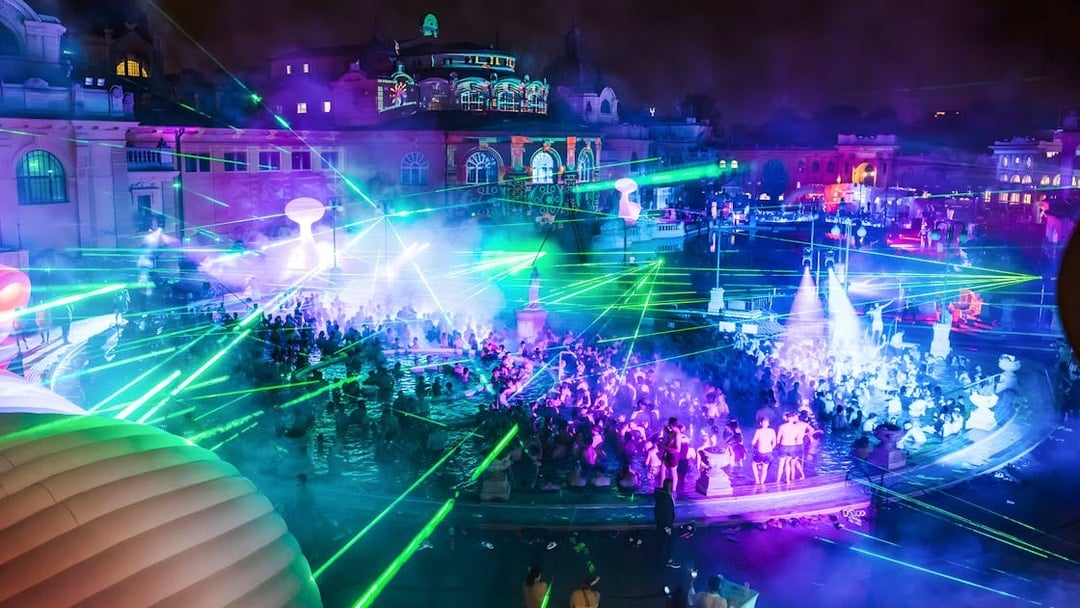 Crowd enjoying Sparty bath party with laser lights at Széchenyi Thermal Bath, Budapest.
