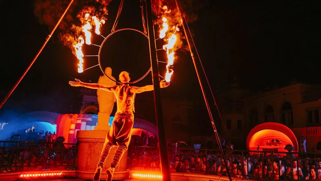 Fire performer at Sparty bath party in Budapest with colorful lights and crowd.