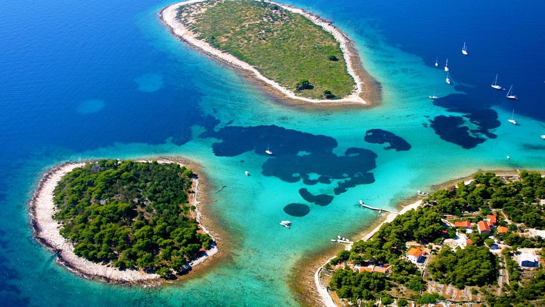 Aerial view of Duga Bay with small islands and sailboats in clear blue water.