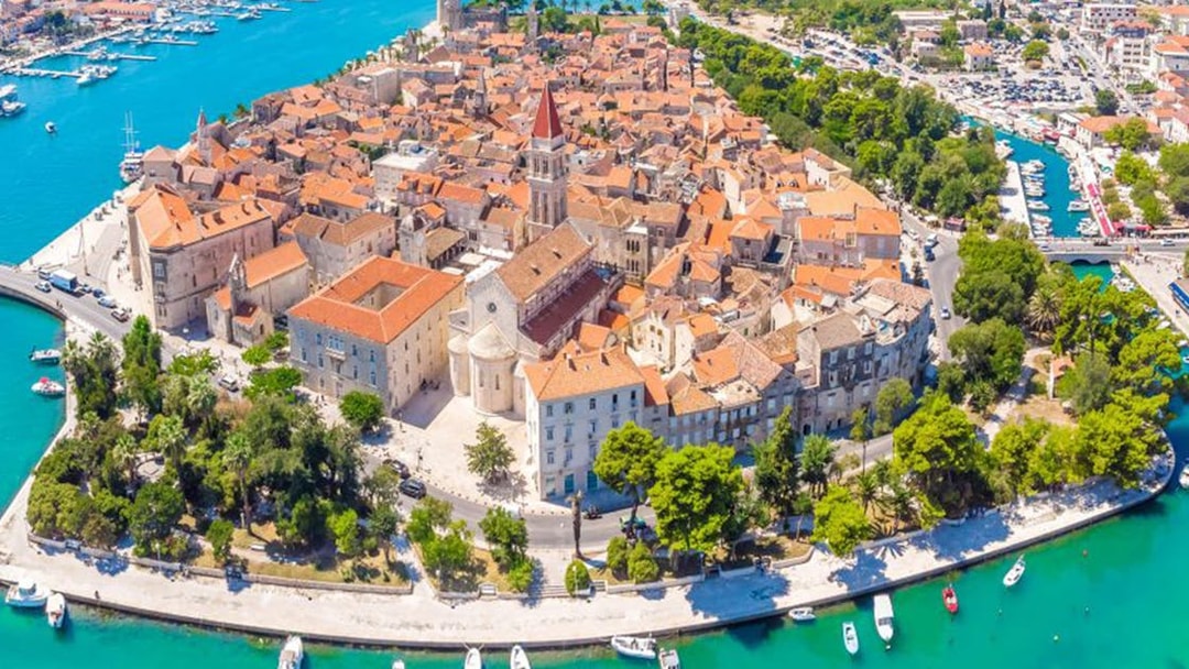 Aerial view of Trogir's historic center with red-roofed buildings and surrounding turquoise waters.