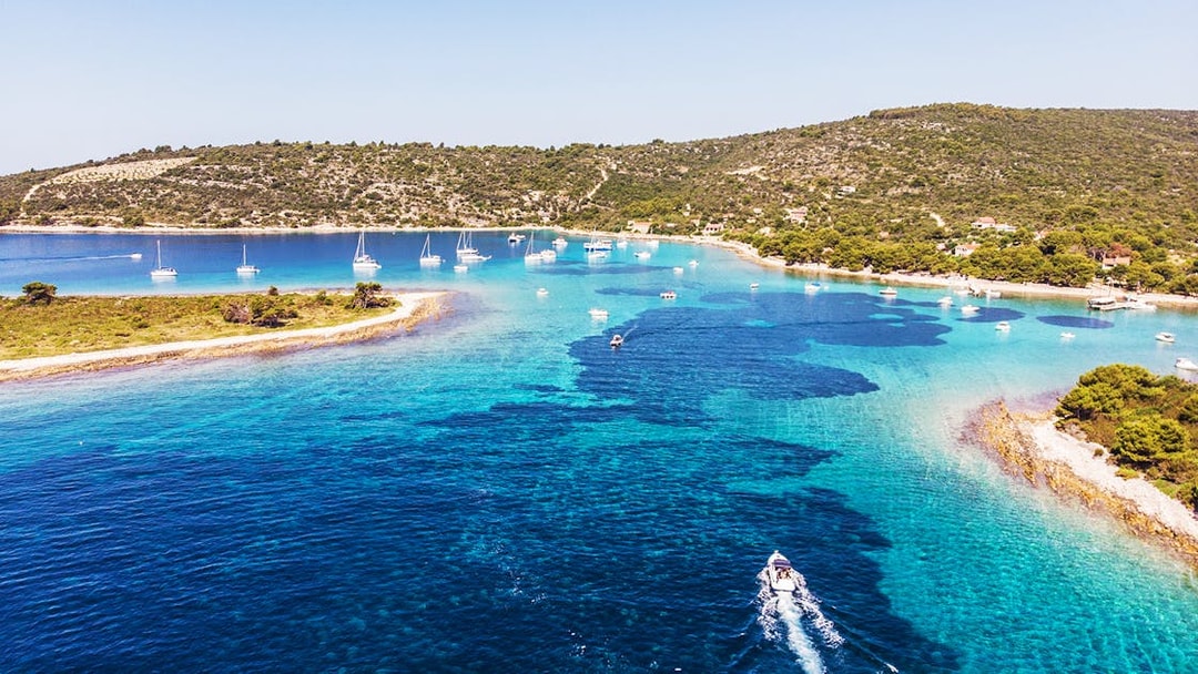 Boats sailing in the clear waters of Blue Lagoon near Split, Croatia, with lush green hills in the background.